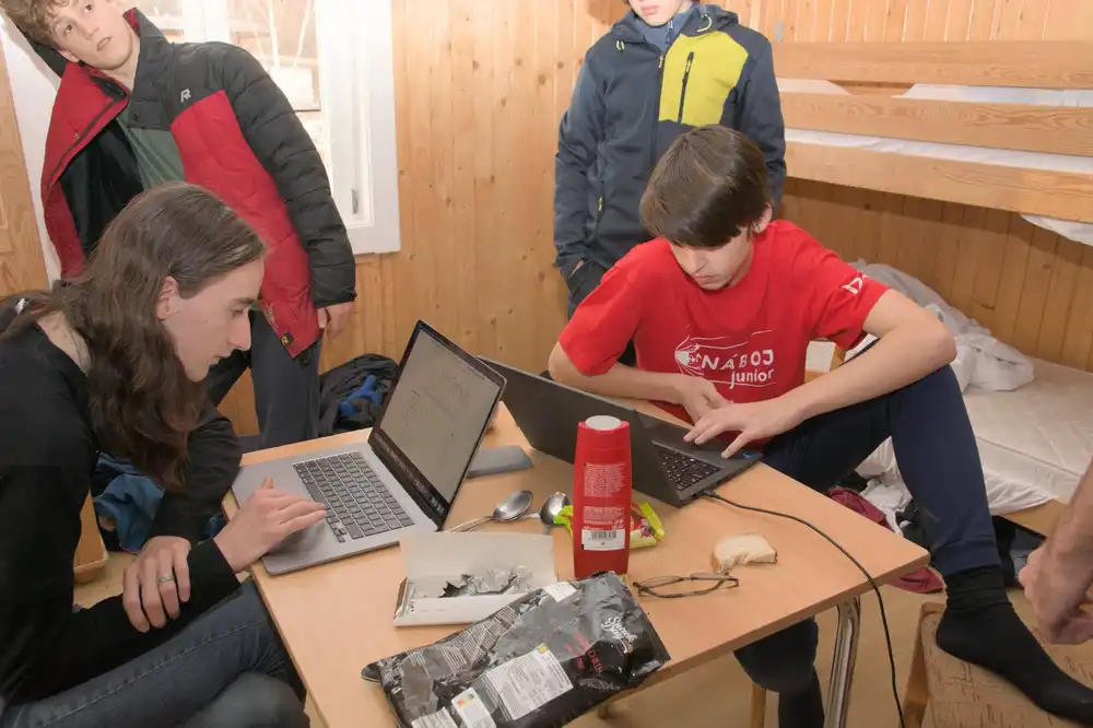 Účastníci sústredenia PRASK sedia pri stole a pracujú na notebookoch